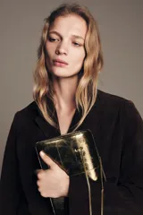 Bolso de hombro de formato rígido en piel metalizada color dorado. Presenta un diseño con pespuntes decorativos, triple compartimento interno y cierre principal mediante imán. Incluye doble asa de hombro en cadena metálica.