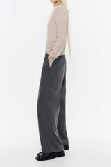 Pantalón negro de corte ancho y tiro alto, con cintura elástica fruncida y pliegues frontales.