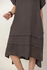 Vestido midi de lino color beige, de corte holgado y silueta acampanada. Cuenta con cuello redondo, mangas cortas amplias, bolsillos laterales y detalles de recortes horizontales en la falda con terminación asimétrica más larga en la parte trasera.