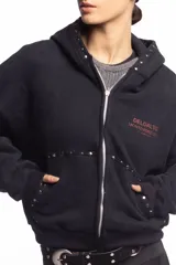 Campera negra de algodón con cierre frontal, capucha, bolsillos laterales y detalles de tachas metálicas en la capucha y los bolsillos. Presenta un estampado frontal con texto en tono rojizo.