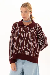 Buzo de punto color vino con diseño de rayas verticales irregulares en tonos claros. Presenta cuello polo con cierre frontal de tres botones, mangas largas con puños acanalados y corte holgado.