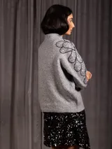 Buzo de cuello alto color gris, de manga larga, con detalle de bordado floral con lentejuelas en el hombro y parte superior de la manga.