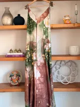 Vestido largo sin mangas con escote en V pronunciado, de corte amplio y fluido, con estampado abstracto en tonos rosados, marrones y blancos, y un cordón trenzado ajustable en la cintura.