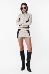 Minifalda deportiva de tiro bajo, color gris con recortes negros y estampa de logo a tono en el recorte trasero. Cierre invisible en el lateral.