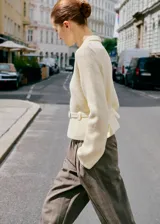 Cardigan de punto color crema con cuello camisero, cierre frontal de cremallera y cinturón integrado con hebilla a la cintura.