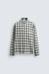 Camisa de corte boxy fit confeccionada en tejido de algodón con elasticidad. Presenta un diseño a cuadros, cuello solapa, manga larga con puños abotonados, bolsillo de vivo en el pecho y cierre frontal con botones.