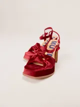 Sandalias de tacón alto Mutma modelo Ñoma, confeccionadas en terciopelo color rojo. Presentan plataforma delantera, taco ancho, tira trasera ajustable con hebilla y diseño de doble nudo en la puntera.