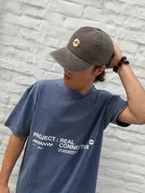 Remera oversize de algodón con efecto acid wash en tono azul oscuro, con estampa blanca en la espalda que incluye los textos "Ost" y "Osten" enmarcados en óvalos, y un diseño de globo terráqueo en el centro.