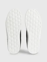 Zapatillas urbanas Calvin Klein con diseño de corte bajo. Presentan una combinación de materiales en la capellada, incluyendo paneles de nailon, cuero y ante en color negro. Destacan por su suela de goma blanca con el logo de la marca estampado en el lateral, forro interior en color azul vibrante y cierre mediante cordones.