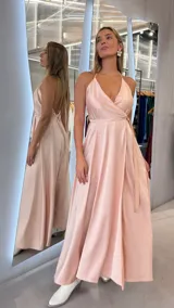 Vestido largo de satén color rosado, con diseño cruzado, escote en V pronunciado, tirantes finos tipo halter y lazo ajustable en la cintura.