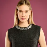 Sweater sin mangas de punto color gris oscuro, con cuello redondo decorado con pedrería brillante tipo joya.