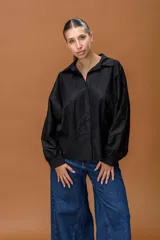 Camisa negra de corte clásico con mangas largas abullonadas y puños abotonados. Presenta paneles de encaje floral en la parte superior delantera y trasera, combinando texturas con un diseño elegante y sofisticado.