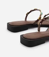 Sandalias planas estilo mule marrones, confeccionadas en PU, con diseño de dedo, dos tiras finas decoradas con aplicaciones de resina y detalles metálicos dorados.