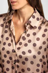 Camisa oversize de poliéster color rosa con estampado de lunares marrón oscuro, cuello camisero, cierre frontal de botones y mangas largas con puños elásticos.
