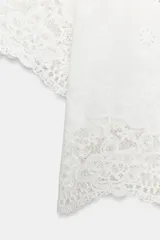 Camisa blanca de manga corta y cuello solapa, con detalles de bordados perforados y encaje en el borde inferior y las mangas. Cuenta con cierre frontal de botones.