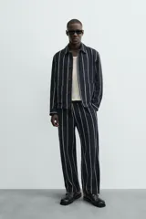 Pantalón de corte relajado, color azul marino, con rayas verticales blancas finas. Presenta cintura elástica ajustable con cordón interior y bolsillos laterales y traseros de plastrón.