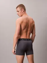 Pack de tres boxers largos Calvin Klein de microfibra, con talle medio y cinturilla elástica distintiva con el logo de la marca. Incluye un bóxer negro con elástico negro y letras blancas, un bóxer gris con elástico negro y letras grises, y un bóxer azul con elástico negro y letras azules.