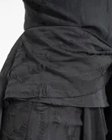 Vestido corto negro de corte asimétrico con escote en V y tirantes finos. Presenta un diseño con efecto desgastado y una sobrefalda con lazo frontal que aporta volumen y movimiento.