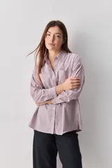 Camisa de calce relajado con diseño a rayas verticales en tonos azul y blanco, cuello clásico, mangas largas con puños abotonados y cierre frontal con botones. Presenta bolsillos aplicados en el delantero y una silueta versátil.