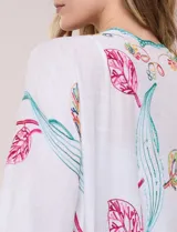 Kimono de poliéster blanco con diseño abierto, mangas amplias y bordados coloridos de motivos florales y arabescos, con terminaciones en ondas de hilo verde.