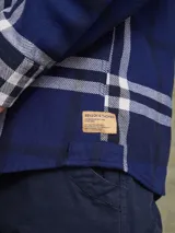 Camisa de manga larga en color azul noche con un patrón de cuadros finos en tonos rojos y verdes. Presenta cuello clásico, cierre frontal con botones y un bolsillo en el pecho con solapa.