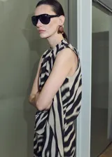 Blusa sin mangas de poliéster con estampado animal print tipo cebra en tonos beige y negro, escote redondo y detalle de volados cruzados en el frente.
