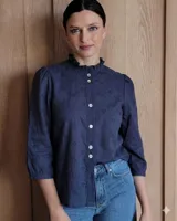 Camisa de algodón con bordado inglés, color azul marino, cuello a la base con volado, cierre frontal con botones y mangas tres cuartos con frunces.