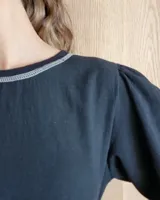 Remera negra de algodón con mangas largas abullonadas y costuras decorativas en contraste en el cuello y el ruedo.