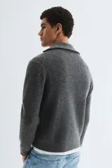 Buzo de punto acanalado en color gris, con cuello elevado y cierre frontal parcial. Presenta un diseño de corte estándar con puños y bajo acanalados.