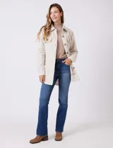 Sobrecamisa de corte amplio confeccionada en tejido suave al tacto, color beige. Presenta cuello de solapa, cierre frontal con botones efecto carey, dos bolsillos frontales con solapa y mangas largas con puños abotonados. El ruedo es redondeado en los laterales y cuenta con canesú en la espalda.