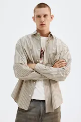 Camisa de popelina de algodón con cuello inglés, tapeta clásica y bolsillo superior abierto. Presenta un canesú en la espalda y mangas largas con puños abotonados. El bajo es levemente redondeado.