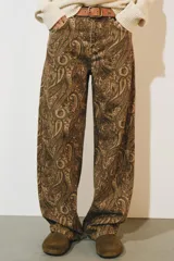 Jeans de tiro medio con diseño de perneras curvas y corte recto, confeccionados en denim con estampado paisley en tonos marrones y beige. Presentan diseño clásico de cinco bolsillos, trabillas para cinturón y cierre frontal con cremallera y botón metálico.
