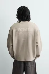 Sudadera de corte boxy fit confeccionada en tejido de mezcla de algodón, con cuello redondo y mangas largas. Presenta un diseño minimalista con texto estampado a contraste en el pecho y efecto lavado.