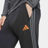 Pantalón de entrenamiento Adidas Tiro25 Essentials, color negro con logo de la marca bordado en naranja. Presenta un ajuste aerodinámico, cintura elástica con cordón y tecnología Aeroready para control de humedad.