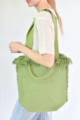 Bolso tipo tote color verde con textura tejida y flecos en los bordes. Tiene doble asa de mano y correa de hombro.