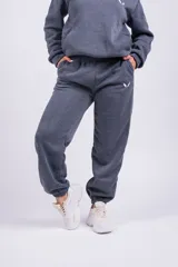 Pantalón de jogging gris oscuro, de corte holgado con cintura elástica y puños ajustados en los tobillos. Presenta bolsillos laterales y un pequeño logo bordado en la pierna izquierda.