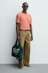 Bolso tipo shopper de algodón en color verde oscuro, con diseño de estampado tipográfico en color crema en el frente. Cuenta con dos asas de mano y cierre magnético.