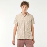 Remera polo de piqué color beige con estampado de palmeras y motivos playeros en blanco.