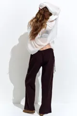 Pantalón marrón de corte holgado con piernas amplias y bolsillos al bies. Modelo de tiro bajo con elástico revestido y cordones para ajustar enlazados a los lados, decorados con cuentas en los extremos.