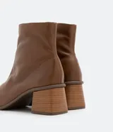 Bota de cuero de caña media para mujer, con punta cuadrada y tacón bloque de 6 cm. Presenta un cierre de cremallera en el lateral interno y una costura central decorativa en la parte frontal.