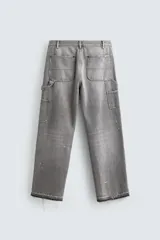 Pantalón de jean estilo carpintero con corte relaxed fit, tiro medio y pierna recta. Presenta un lavado azul medio con efecto desgastado y roturas en las rodillas. Incluye bolsillos laterales tipo plastrón, tira multifunción en la pierna, cierre frontal con cremallera y botón.