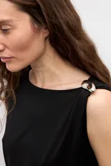 Blusa blanca de manga corta y corte recto, con escote bote y detalle metálico circular en el hombro.