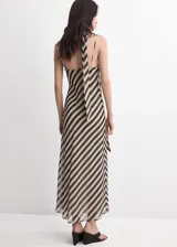 Vestido largo de fiesta con diseño de rayas diagonales en tonos beige y negro. Cuenta con tirantes finos, cuello drapeado y un adorno de fular incorporado en el cuello.