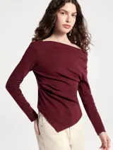 Blusa negra de manga larga con diseño asimétrico en el escote, dejando un hombro al descubierto. Presenta un corte ajustado con detalle de frunces laterales que crean un efecto drapeado en el torso.