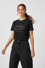 Remera de algodón negra con cuello redondo y mangas cortas. Presenta un estampado frontal con tipografía cursiva y letras en color rosado.