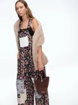 Mono de estilo jardinera con estampado floral y detalles de parches en diferentes texturas y patrones. Presenta un bolsillo frontal en color claro, tirantes ajustables con hebillas metálicas y piernas de corte recto y holgado.