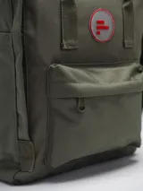 Mochila color verde militar con diseño clásico y minimalista. Cuenta con un compartimento principal con cierre de doble cremallera, un bolsillo frontal con cierre y dos asas superiores con broche. En el frente, tiene un parche circular con el texto "FORUM INDUSTRIES CO." en rojo.