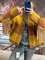 Campera de lana italiana con diseño de cuadros en tonos amarillo y marrón. Presenta flecos de gamuza en las mangas, cierre frontal y bolsillos laterales. La prenda se encuentra completamente forrada.