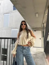 Blusa color crema con escote halter y diseño strapless con hombros descubiertos, mangas largas abullonadas con puños elastizados y corte corto.