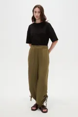 Pantalón verde militar de corte ancho y tiro alto, con cintura elástica fruncida y detalles de cordones ajustables en los tobillos.